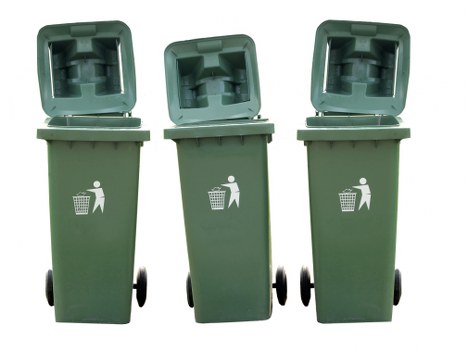 Three green wheeled rubbish bins with hinged, open lids are positioned upright on a paved outdoor surface, visible from a frontal perspective. The bins are made of durable plastic with textured finish and feature white pictograms of a person disposing of waste, indicating their use for general rubbish collection. They are arranged in a row with slight spacing, and the background is plain and neutral, suggesting an outdoor setting such as a driveway or pavement near a commercial or residential property. The open lids reveal the hollow interior of each bin, designed to hold waste materials. The environment appears clean and well-maintained, with the bins aligned in preparation for rubbish removal services. This visual is representative of waste management practices in Woolwich or nearby areas, as undertaken by Commercial Waste Removal Woolwich, and is relevant to the service category of rubbish collection and business clearance in London’s southeast boroughs.